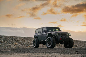 日落時分，一輛灰色Jeep Wrangler停在岩石山坡上。