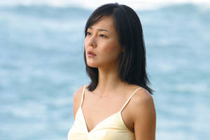 一位身穿黃色泳衣的女性站在海邊，若有所思。