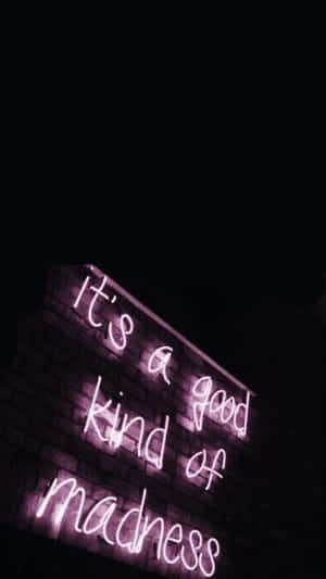 磚牆上的紫色霓虹燈牌在夜晚顯示 'it's a good kind of madness'。 — iPhone 8 壁紙