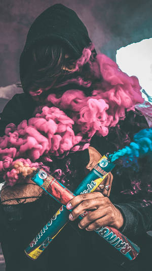 穿著黑色連帽衫的人手持煙霧彈，釋放出粉紅色和藍色煙霧。 — 食草 壁紙