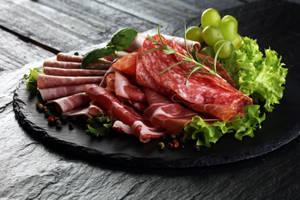 深色石板上的醃製肉類、葡萄、生菜和香草拼盤
