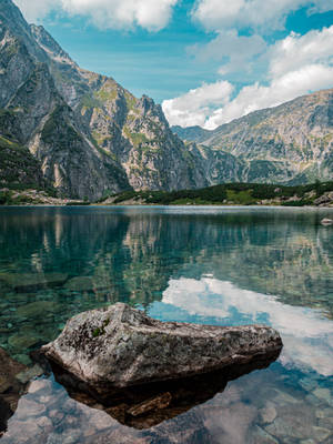 山湖清澈的水面反射出雲朵和岩石山峰，在藍天下