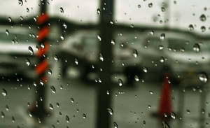 窗戶上的雨滴，俯瞰一條模糊的街道，有汽車和橙色錐體。