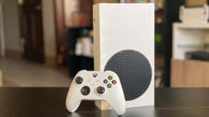 白色 Xbox Series S 主機和手掣在室內深色桌子上。