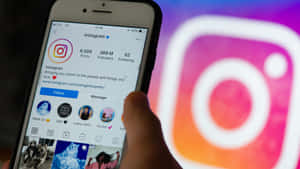 手拿著電話顯示Instagram個人資料，背後有模糊的應用程式標誌。