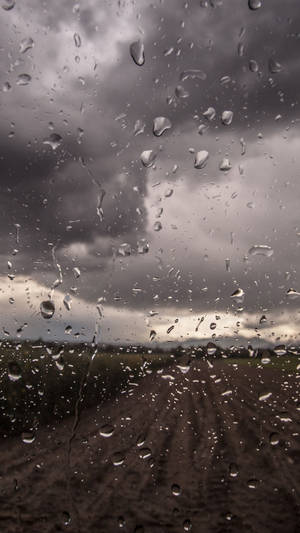 車窗上的雨滴，俯瞰暴風雨天空下的泥濘田野。