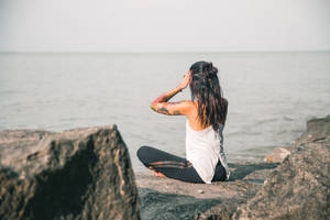 有紋身的女性坐在岩石上，面向日落時分的海洋。 — 海洋 壁紙