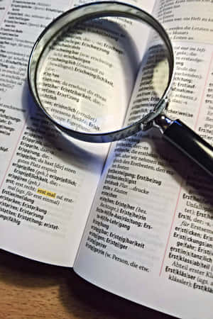 放大鏡聚焦喺木枱上嘅德文字典中「erstmal」嘅詞條。 — 工具 壁紙