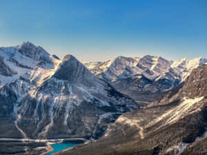 晴朗藍天下，森林山谷中帶有碧綠湖泊的白雪覆蓋山脈。