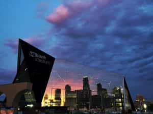 黃昏時分的 US Bank Stadium，城市燈光倒映在玻璃外牆上。