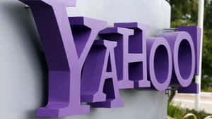 灰色建築物上的紫色 Yahoo 標誌，附近有綠色植物。