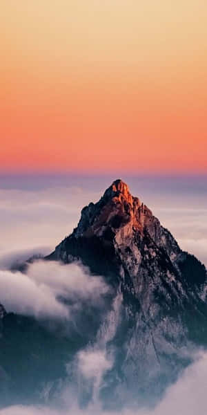 日落時分，橙色和粉紅色的天空下，山峰聳立於雲層之上。