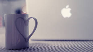 白色心形馬克杯放在Apple筆記本電腦旁邊，條紋桌面。