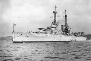 一艘大型戰艦在多雲的天空下停泊在平靜的水域中。 — 現代戰爭 壁紙