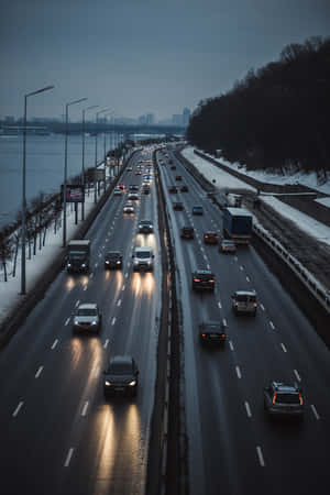 積雪的高速公路，汽車在黃昏時分行駛，靠近河流和城市天際線。 — 暮光 壁紙