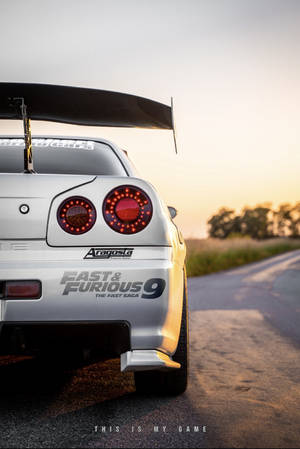 一輛帶有『狂野時速9』貼紙的銀色日產Skyline GT-R，停在日落時分的鄉村道路上。