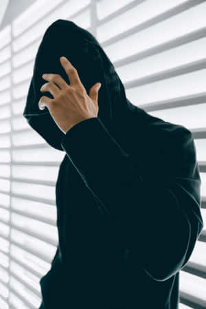 穿著黑色連帽衫的人在窗簾附近將帽子拉過臉部