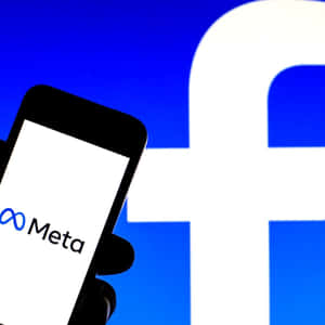 手拿著手機，手機上有Meta標誌，前面有Facebook標誌。