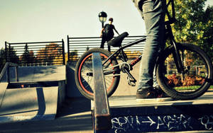 BMX單車靠在滑板公園欄杆上，車手在附近，秋日陽光