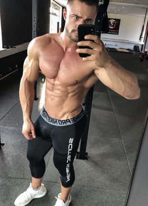 肌肉發達的男士在健身房穿著黑色緊身褲和白色運動鞋對著鏡子自拍。