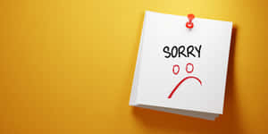 一張寫有「SORRY」和悲傷臉孔的便利貼，釘在黃色牆上。