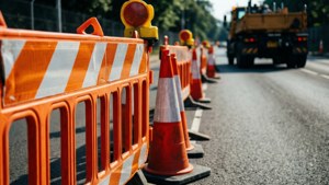 陽光道路上帶有建築卡車的橙色交通錐和屏障。