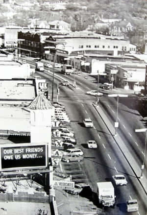 1960年代繁忙城市街道的鳥瞰圖，有復古汽車和商店門面。 — 黑白 壁紙