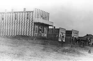 歷史格子建築，人們在塵土飛揚的小鎮中靠近沙龍招牌。 — 黑白 壁紙