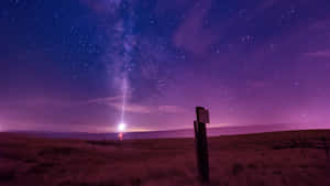 一個人在沙漠中，站在可見銀河的紫色星空下。 — 月色夜空 壁紙