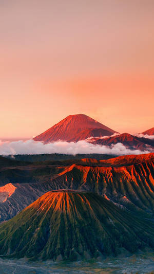 日出時的火山山脈，下方的雲朵在橙色和粉紅色的光芒中閃耀。
