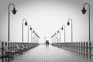 兩人在雨中木碼頭上撐傘行走，旁邊有燈柱。