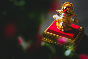 金色象神雕像在紅色軟墊底座上，帶模糊花卉背景。