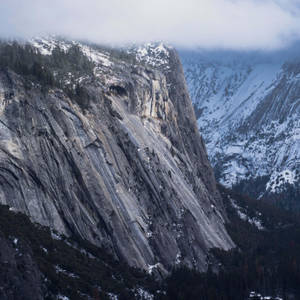 積雪的花崗岩山峰部分被雲和常綠樹覆蓋。