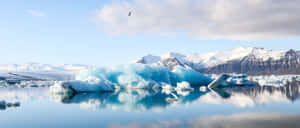 冰山漂浮在平靜的水面上，背景是積雪覆蓋的山脈。 — 美學 壁紙