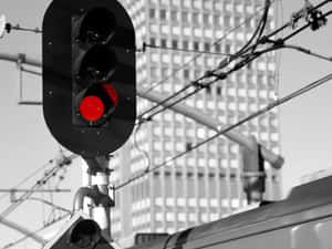 黑白城市景觀中的紅色火車信號燈，帶有架空電線和經過的火車。