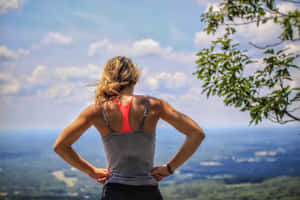 一位穿著運動服的女士站在山頂上，俯瞰著風景如畫的山谷。