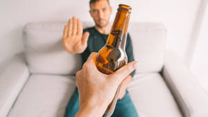 手拿啤酒瓶，沙發上的男人用手掌阻止它。 — 男人 壁紙