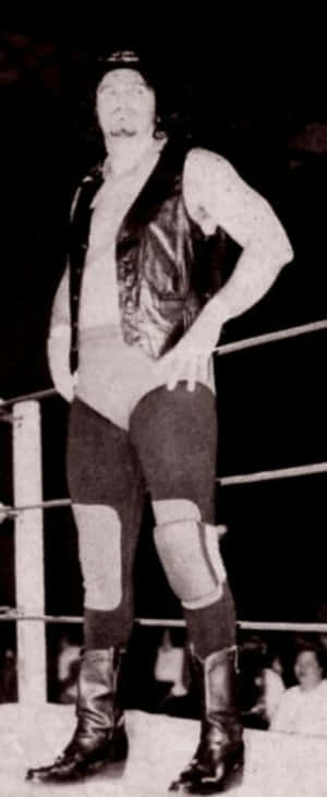 一名摔角手穿著皮背心和靴子在摔角擂台上擺姿勢。 — 黑白 壁紙