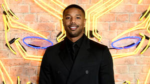 Michael B Jordan 身穿黑色西裝，對著鏡頭微笑，身後有霓虹燈。 — 邁克爾·喬丹 壁紙