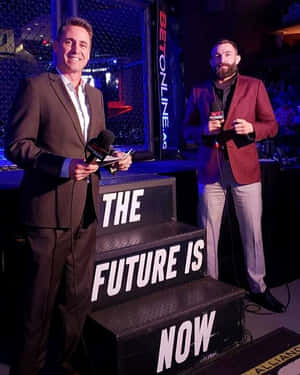 兩位UFC評論員在舞台上，身後有「The Future Is Now」階梯。
