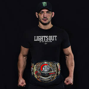 一位MMA冠軍戰士佩戴冠軍腰帶，身穿印有「Lights Out」字樣的黑色T恤。