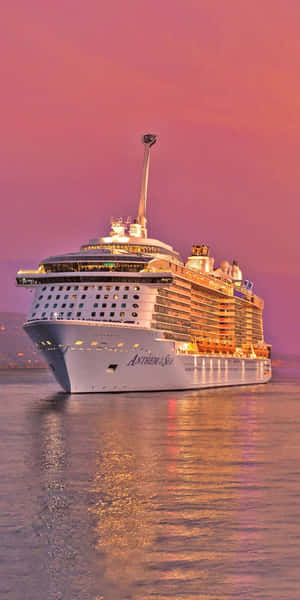 一艘名為 Anthem of the Seas 的大型郵輪在黃昏時分航行，伴隨著粉紅色的天空和水面倒影。 — 日落天空 壁紙