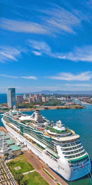 一艘大型郵輪停靠在沿海城市，擁有現代建築和藍色海洋，在晴朗的天空下。 — 藍天 壁紙