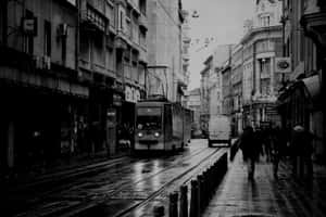 雨中的城市街道，有電車和人們在濕漉漉的鵝卵石上行走。