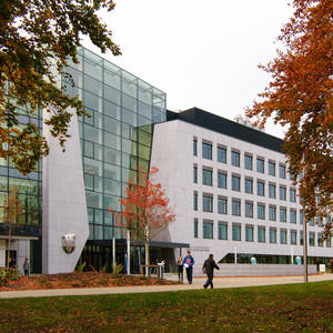 現代大學建築，玻璃和石材外牆，周圍有秋樹和走路的學生。