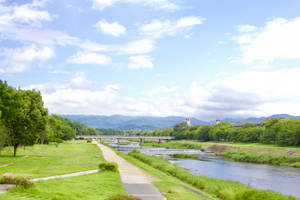 一條河流流經一個綠色公園，有小徑和遠處的山脈，在藍天下。
