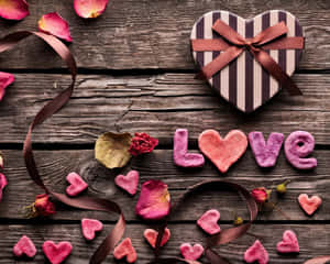 心形禮物盒和粉紅色黏土心形在木桌上拼出 love，並有玫瑰花瓣。