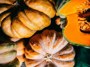 各種南瓜和 squash 呈現秋季色彩，紋理外皮和一個切半的南瓜顯示橙色果肉。 — 南瓜 壁紙