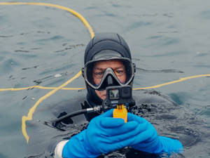 潛水員手持GoPro相機在水面上方，身後拖著黃色繩索 — 相機 壁紙