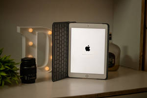 iPad 配備鍵盤保護套，顯示 Apple 標誌，旁邊有發光字母 D 相機鏡頭和植物。
